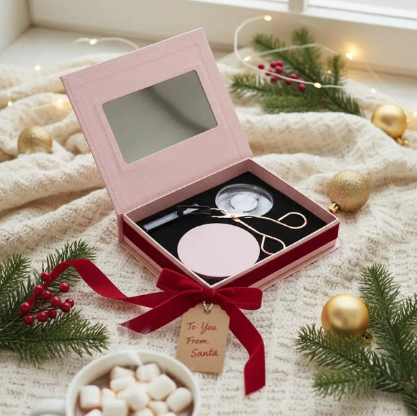 Cosmetic set in a pink box with a red ribbon and 'To You From Santa' tag, surrounded by Christmas decorations.
